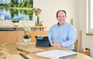 tischlerei-woehltjen-tischlerei-achim-stephan-woehltjen Stephan Wöhltjen sitzt an einem Holztisch. Vor ihm steht ein Tablet